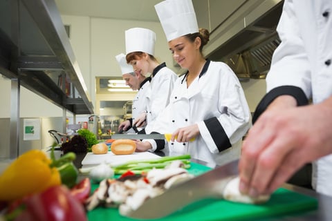 Four chefs preparing food at counter in a row in a professional kitchen
